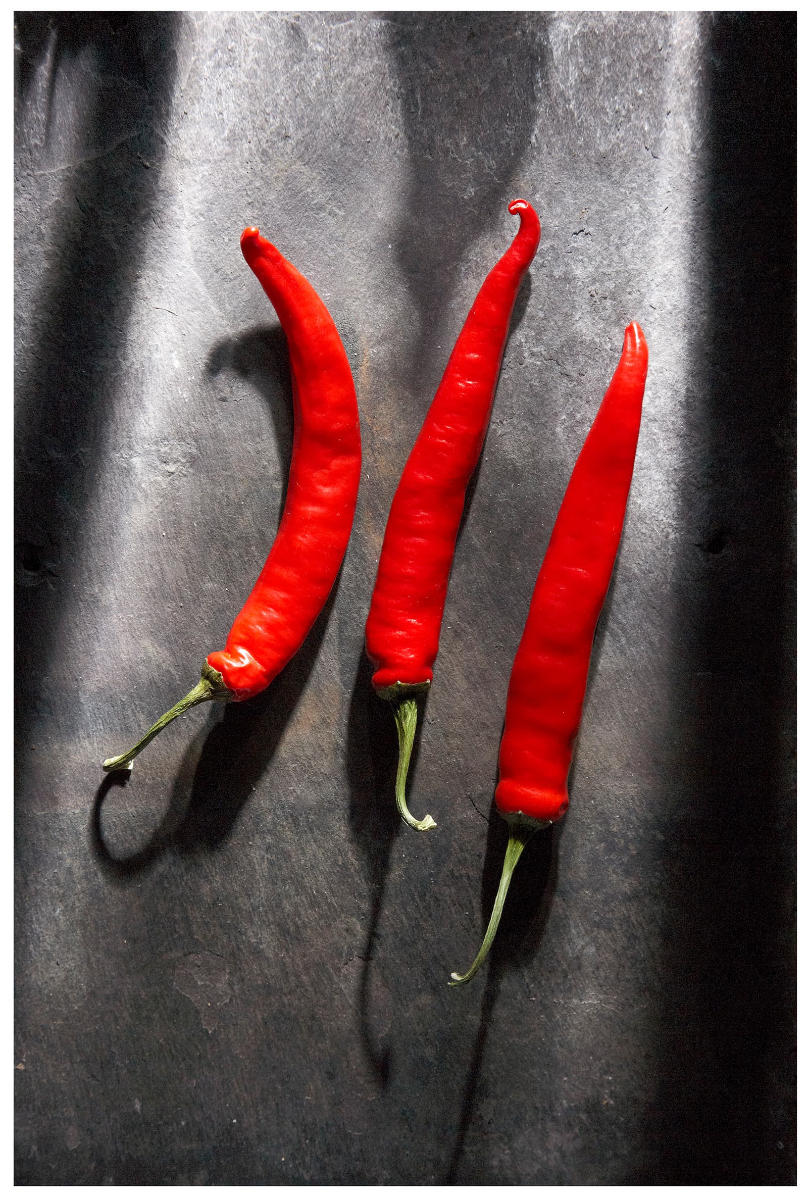Still life of three red chillies on dark slate