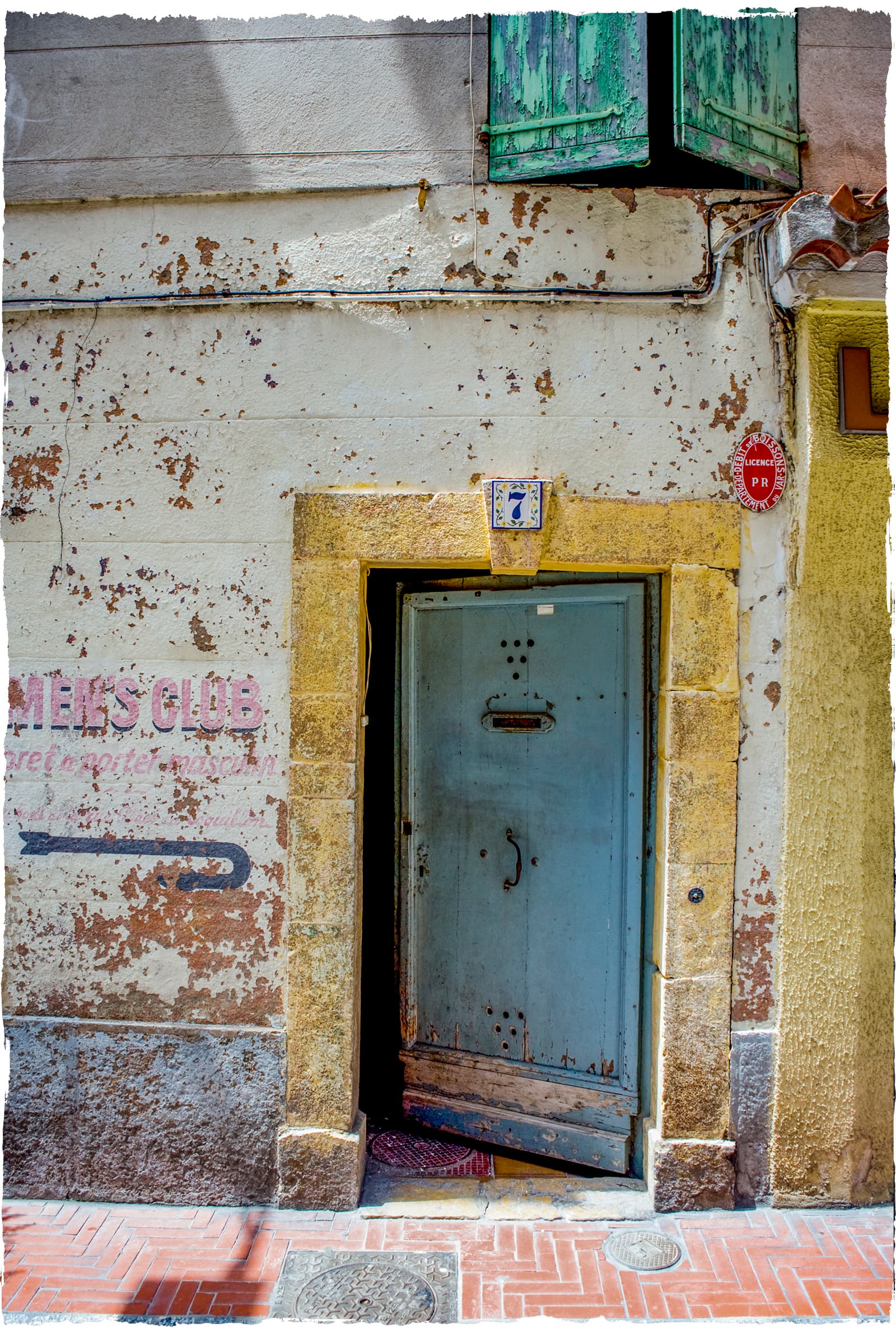 Faded 'Men's Club' shop signage beside a weathered doorway in Sanary-sur-Mer