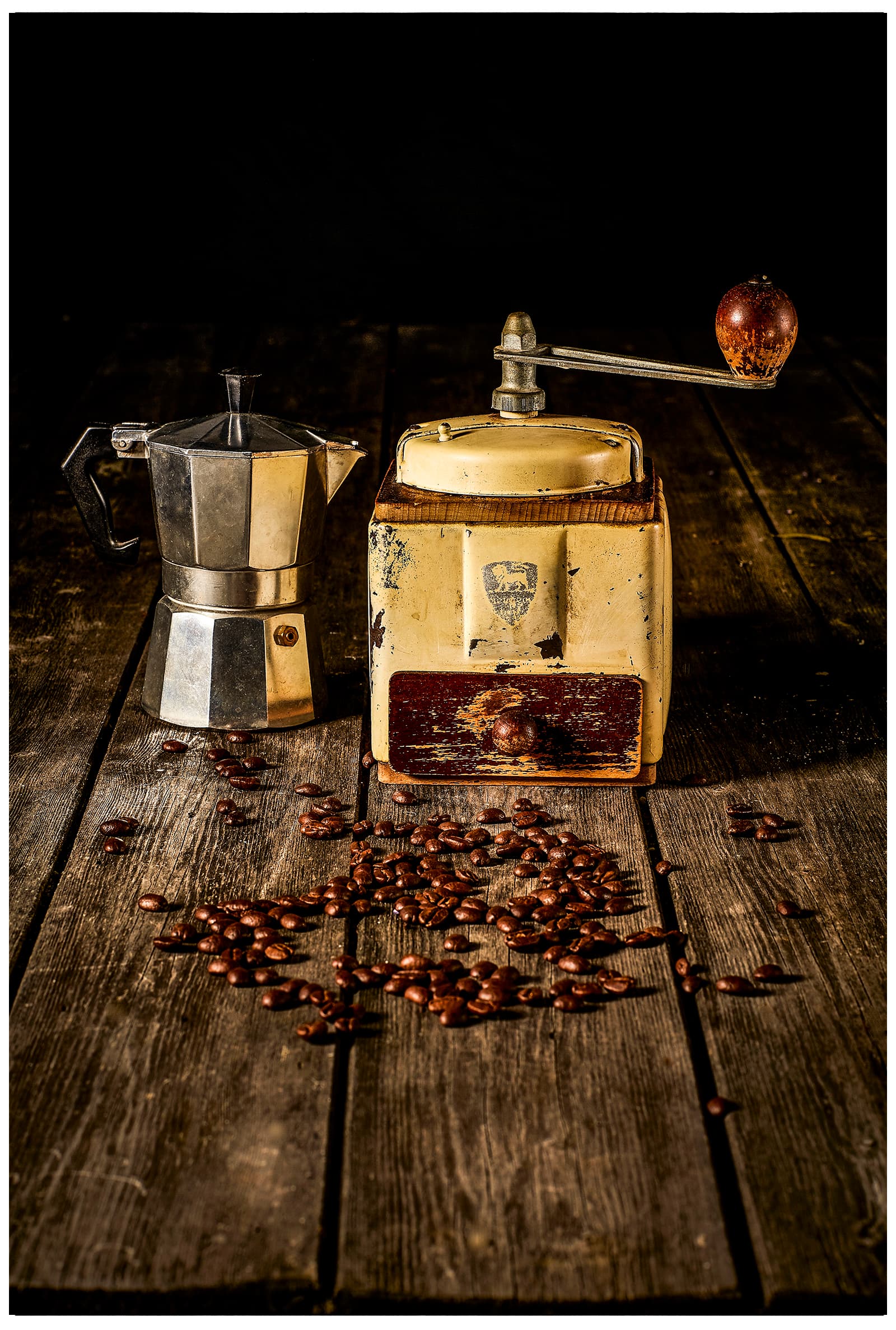 Still life of a vintage Peugeot coffee grinder, moka pot and scattered coffee beans