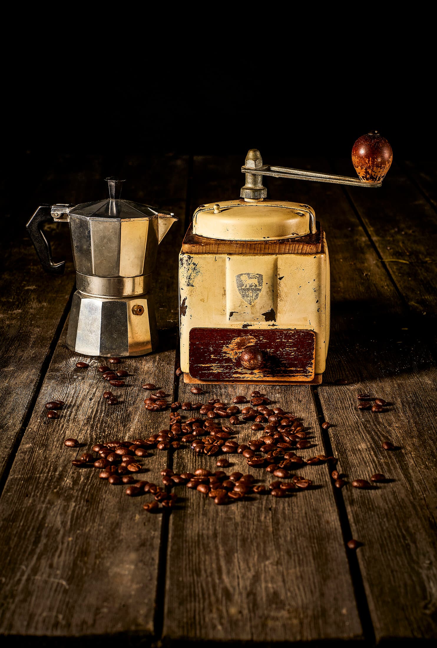 Still life of a vintage Peugeot coffee grinder, moka pot and scattered coffee beans