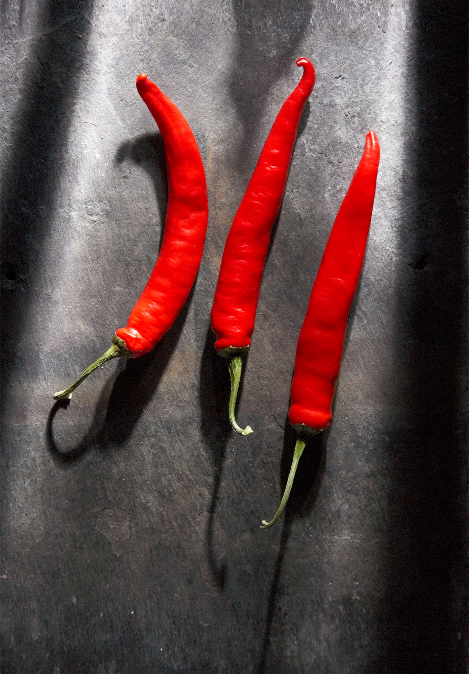 Still life of three red chillies on dark slate