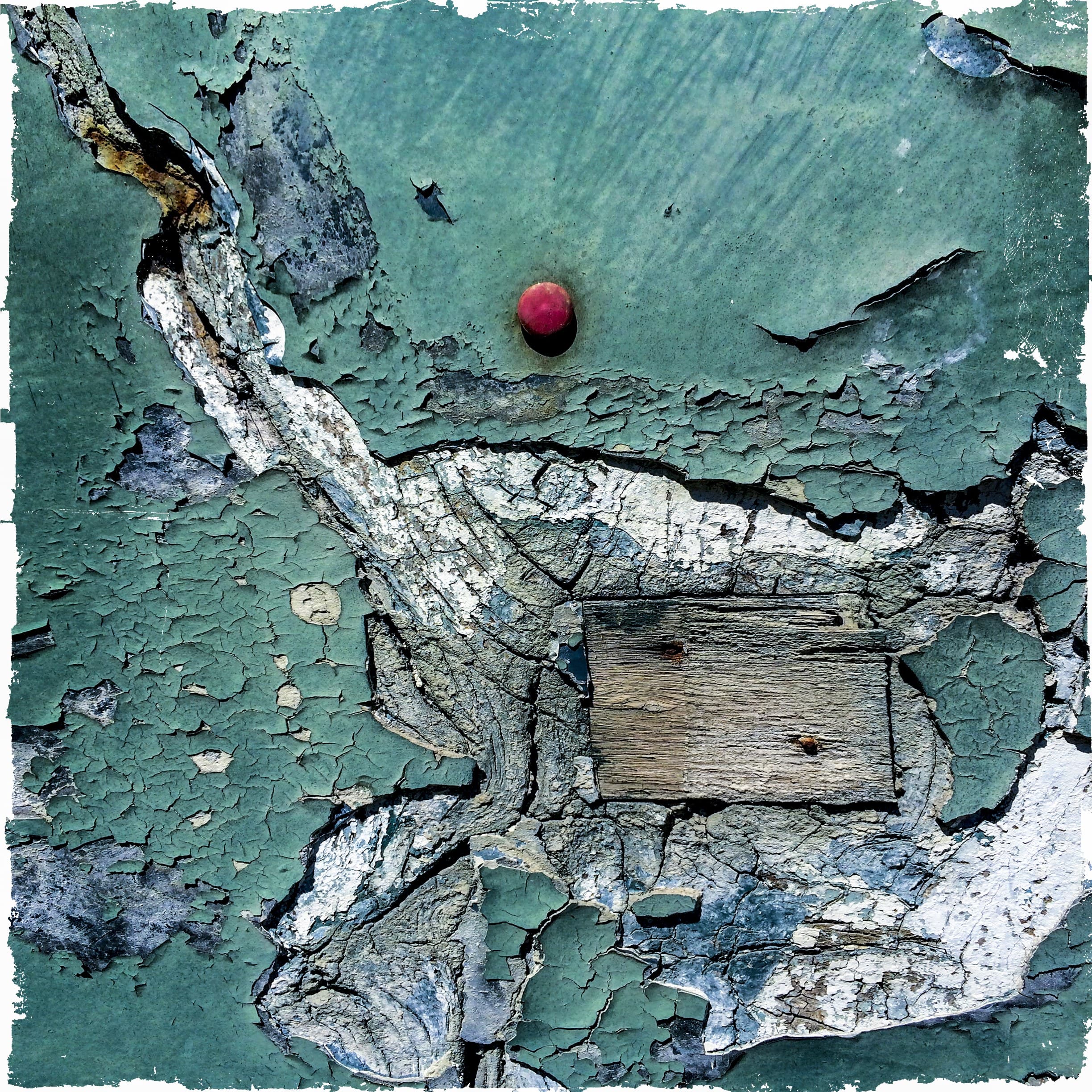 Peeling teal paint on an old door in Antibes, with a red drawing pin and a patch of bare wood